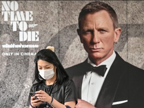 A woman wearing a face mask amid fears of the spread of the COVID-19 novel coronavirus walks past a poster for the new James Bond movie "No Time to Die" in Bangkok on Feb. 28, 2020. (MLADEN ANTONOV/AFP via Getty Images)