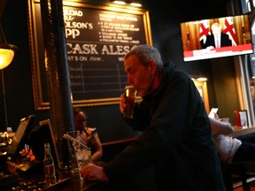A man with a drink as Britain's Prime Minister Boris Johnson, is seen on a television screen in a pub in London as the spread of the coronavirus disease (COVID-19) continues. In Westminster, London, Britain March 20, 2020. (REUTERS/Hannah McKay)