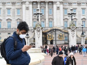 A tourist wearing a mask checks his cellphone in front of Buckingham Palace in London, England, on Saturday, March 14, 2020.