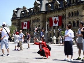 Canadian flags are seen on the Office of the Prime Minister and Privy Council as tourists take photos on Parliament Hill before Canada Day, in Ottawa on June 27, 2019.