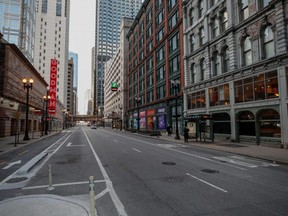 A woman waits for a bus on a nearly empty street in downtown Chicago, Saturday, March 21, 2020.