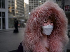 A Chinese woman wears a protective mask with her hood pulled up as she leaves an office building in Beijing's central business district, on Thursday, March 12, 2020.