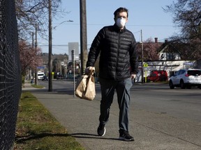 A man wears a mask along Cook St. where the COVID-19 drive-thru testing clinic which was recently launched across the street by Island Health in Victoria, B.C., on Friday, March 20, 2020.