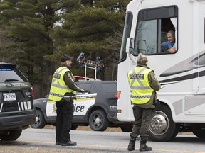 Members of Quebec's provincial police force talk to the driver of a recreational vehicle near the border of the United States in Saint-Bernard-de-Lacolle, south of Montreal, Saturday, March 28, 2020, as Coronavirus COVID-19 cases rise in Canada and around the world.