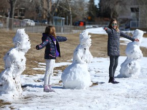 Sisters Mallory Hagg, 8, and Claudia Hagg, 11 have some fun with social distancing while they check out three snowmen in Meadowlark Park on 5 St SW in Calgary on Sunday, March 22, 2020. Jim Wells/Postmedia