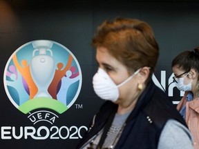Travellers pass by a logo of the 2020 UEFA European Football Championship displayed on a wall inside Bucharest Henri Coanda International Airport, in Otopeni, Romania, Monday, March 16, 2020.