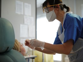 A medical worker wearing protective mask and suit performs a test on a woman suspected to be infected at the hospital in Vannes where patients suffering from coronavirus disease (COVID-19) are treated, France, March 20, 2020. (REUTERS/Stephane Mahe)