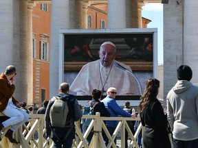 People watch a screen live-broadcasting Pope Francis' Sunday Angelus prayer on St. Peter's Square at the Vatican on March 8, 2020, after millions of people were placed under forced quarantine in northern Italy as the government approved drastic measures in an attempt to halt the spread of the COVID-19 outbreak, caused by the novel coronavirus that is sweeping the globe.