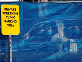 Medical staff assess people for coronavirus disease (COVID-19), as seen through a mesh tarp, at the public Victoria Health Unit in Victoria, British Columbia, Canada March 17, 2020.