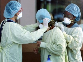 Health care workers help a visitor going to the intensive care unit put on a gown and mask to protect against contracting Severe Acute Respiratory Syndrome (SARS) at North York Hospital in Toronto, May 29, 2003.