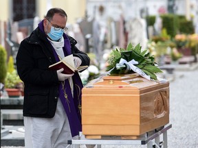 A priest wearing a face mask checks a book of funeral rites as he gives the last blessing to a deceased person, by a coffin during a funeral ceremony outside the cemetery of Bolgare, Lombardy, on March 23, 2020 during the COVID-19 pandemic.