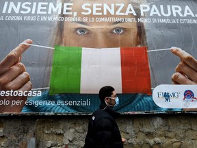 A man walks past a large billboard raising awareness to the measures taken by the Italian government to fight against the spread of the novel coronavirus which pictures a woman wearing Italy's flag as a facemask and reads "All together, without fear", in Naples on Sunday, March 22, 2020.