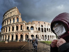 A man wearing a protective mask passes by the Coliseum in Rome on March 7, 2020 amid fear of COVID-19 epidemic.