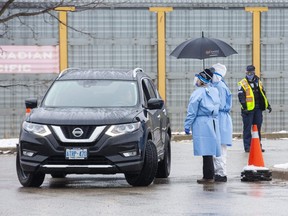 Health-care workers use an umbrella to stay dry while speaking to people in their cars at the Carling Heights Optimist Community Centre COVID 19 assessment centre in London, Ont. on Monday March 23, 2020.