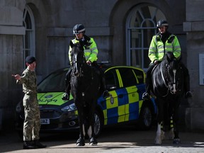 Police officers on horses talk to a member of the army in London March 24, 2020. (REUTERS/Hannah McKay)