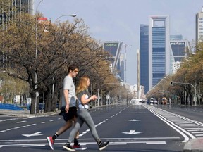 Two people cross the usually busy La Castellana avenue in Madrid on Sunday, March 15, 2020.