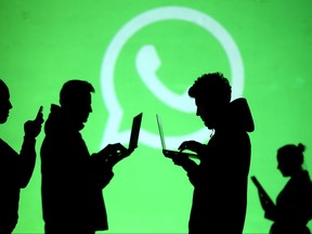 Silhouettes of laptop and mobile device users are seen next to a screen projection of Whatsapp logo in this picture illustration taken March 28, 2018.  (REUTERS/Dado Ruvic/Illustration/File Photo)
