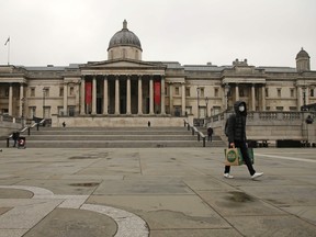 A man wearing a face mask as a precautionary measure against COVID-19 coronavirus carries shopping bags as he walks across a deserted Trafalgar Square in London, England on Thursday, March 19, 2020.
