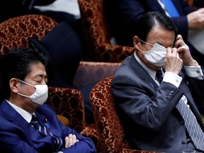 Japan's Finance Minister Taro Aso, next to Japan's Prime Minister Shinzo Abe, adjusts his protective face mask during an upper house parliamentary session, following an outbreak of the coronavirus disease (COVID-19), in Tokyo, Japan April 1, 2020. (REUTERS/Issei Kato)