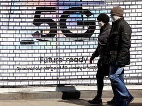 People wearing masks walk past a 5G advert as the spread of the coronavirus continues in London April 14, 2020.