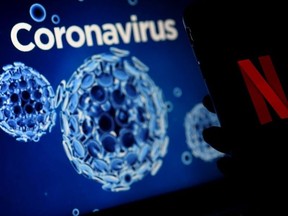 In this file photo illustration taken on March 31, 2020, a mobile phone screens display the Netflix logo next to a coronavirus, COVID-19, illustration graphic background in Arlington, Virginia.