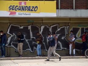 A group of mene wearing face masks as a preventive measure against the spread of the coronavirus queue waiting for their turn to enter a bank in Bogota on April 13, 2020.