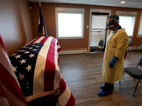 Michael Neel, funeral director of of All Veterans Funeral and Cremation, wearing full PPE, looks at the U.S. flag on the casket of George Trefren, a 90 year old Korean War veteran who died of COVID-19 in a nursing home, in Denver, on Thursday, April 23, 2020.