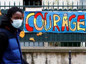 A man wearing a protective mask walks past a sign that reads "Courage", in Paris as a lockdown is imposed to slow the rate of COVID-19 in France, on Saturday, April 25, 2020.