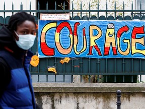 A man wearing a protective mask walks past a sign that reads "Courage", in Paris as a lockdown is imposed to slow the rate of the coronavirus disease (COVID-19) in France, April 25, 2020.