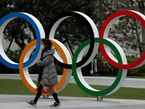 FILE PHOTO: A woman wearing a protective face mask, following an outbreak of the coronavirus disease (COVID-19), walks past the Olympic rings in front of the Japan Olympics Museum, in Tokyo, Japan March 30, 2020. REUTERS/Issei Kato/File Photo ORG XMIT: FW1