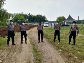 This handout picture taken and released by Indonesia Police on April 5, 2020 shows policemen wearing face masks at a cemetery in Jakarta, as they guard workers and family members during funerals for victims of the COVID-19 coronavirus. (HANDOUT/INDONESIAN POLICE/AFP via Getty Images)