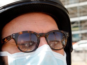 A construction site is reflected on the sunglasses of a man wearing a protective mask as the spread of COVID-19 continues, in Naples, Italy, Friday, April 17, 2020.
