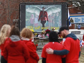 Mourners, asked to wear red on Friday, are seen near a mural dedicated to slain RCMP Const. Heidi Stevenson, during a province-wide, two-minutes of silence for the 22 victims of last weekend's shooting rampage, in front of the RCMP detachment in Cole Harbour, N.S., on Friday, April 24, 2020.