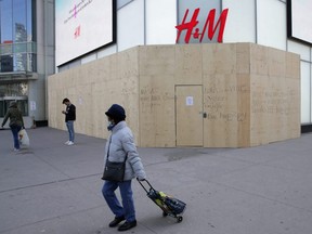 A woman wearing a protective face mask passes the closed and boarded up H&M clothing store at the Eaton Centre in downtown Toronto during the global outbreak of COVID-19, April 6, 2020.