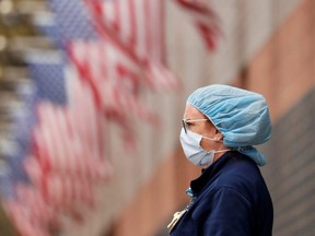 A nurse wearing personal protective equipment watches an ambulance driving away outside of Elmhurst Hospital during the ongoing outbreak of COVID-19 in the Queens borough of New York City, April 20, 2020.