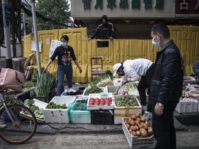 A vendor sells vegetables in front of a makeshift barricade built to control entry and exit to a residential compound in Wuhan, Hubei Province, China, on Friday, April 17, 2020.