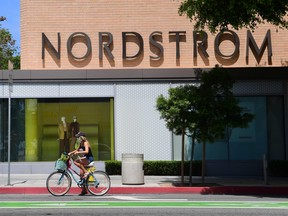 A pedestrian and cyclist wear face masks outside a branch of department store chain Nordstrom in Santa Monica, California on May 11, 2020.