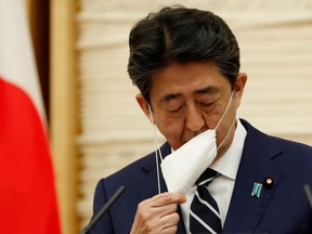 Japan's Prime Minister Shinzo Abe removes his face mask as he starts a news conference in Tokyo on May 25, 2020.