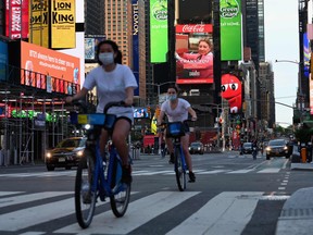 In this file photo taken on May 27, 2020 people wearing a face masks ride their bikes through Times Square in New York City, amid the novel coronavirus pandemic.