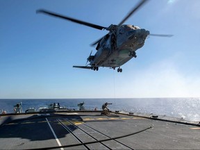 Air detachment members aboard HMCS Fredericton attach a fueling hose on the hoist cable of a CH-148 Cyclone helicopter during Operation Reassurance at sea February 15.