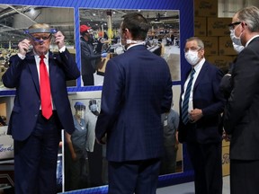 U.S. President Donald Trump holds up a protective face shield as Ford Motor Company executives wearing face masks look on during a tour of the Ford Rawsonville Components Plant that is manufacturing ventilators, masks and other medical supplies during the COVID-19 pandemic, in Ypsilanti, Michigan, Thursday, May 21, 2020.