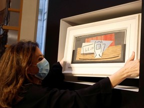 Raffle organizer Peri Cochin, wearing a protective face mask, poses with the painting "Nature Morte, 1921" by Spanish painter Pablo Picasso after the charity raffle official draw to designate the winner of the Picasso oil painting for 100 euros at Christie's auction house in Paris, May 20, 2020.