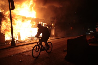 A man rides a bicycle past a burning building during protests sparked by the death of George Floyd while in police custody on May 29, 2020 in Minneapolis, Minn.