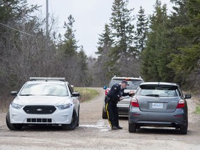 An RCMP officer talks with a local resident before escorting them home at a roadblock in Portapique, N.S. on Wednesday, April 22, 2020.