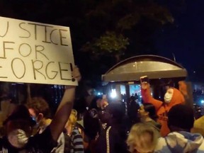 A demonstrator holds a placard while protesters gather around an on fire entrance of a police station, as demonstrations continue after a white police officer was caught on a bystander's video pressing his knee into the neck of African-American man George Floyd, who later died at a hospital, in Minneapolis May 28, 2020, in this picture grab obtained from a social media video.