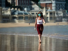 A woman wearing a face mask strolls on La Concha beach in San Sebastian, on May 2, 2020, during the hours allowed by the government to exercise.