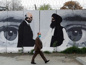 An Afghan man wearing a face mask walks past a wall painted with photo of Zalmay Khalilzad, U.S. envoy for peace in Afghanistan, and Mullah Abdul Ghani Baradar, the leader of the Taliban delegation, in Kabul, Afghanistan April 13, 2020.