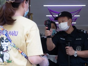 A security guard checks the body temperature of a woman in Wuhan in China's central Hubei province on Monday, May 11, 2020.