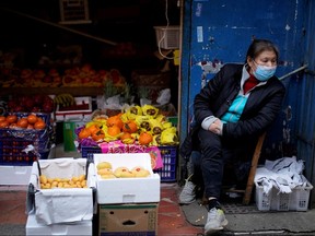 A woman wearing a face mask sits next to a fruit stall at a residential area after the lockdown was lifted in Wuhan, April 11, 2020.