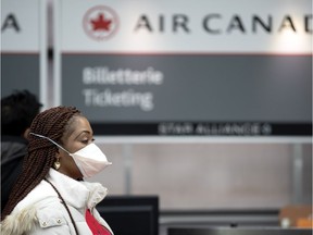 A woman covers her face with a mask as she waits at the Air Canada ticketing counter at Pierre Elliott Trudeau Airport in Montreal, on Wednesday, March 11, 2020.